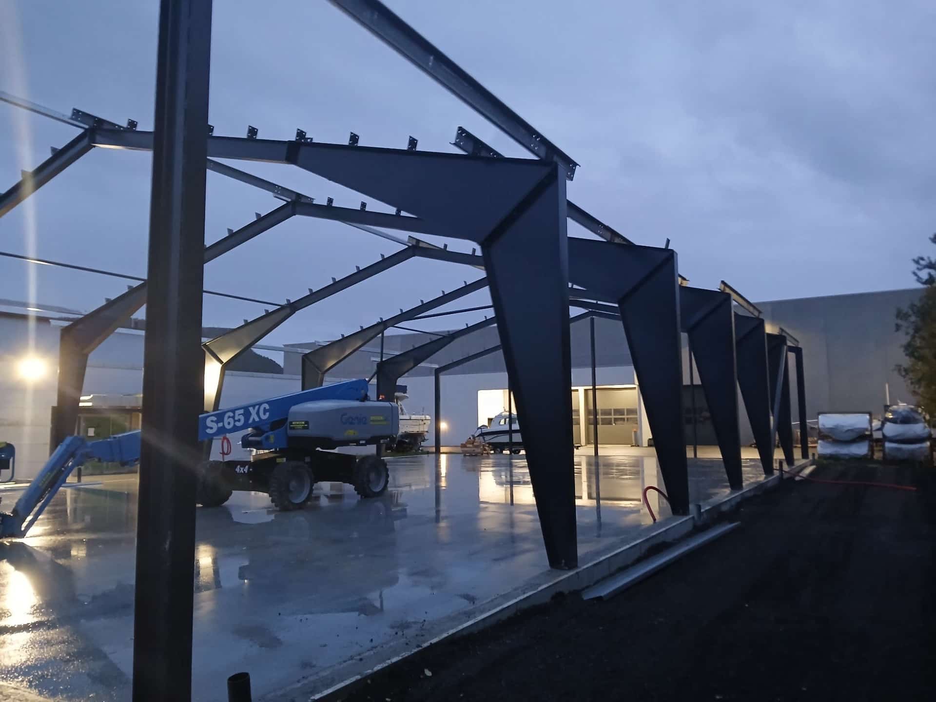 Newly erected steel portal frames at dusk, with a boom lift on site