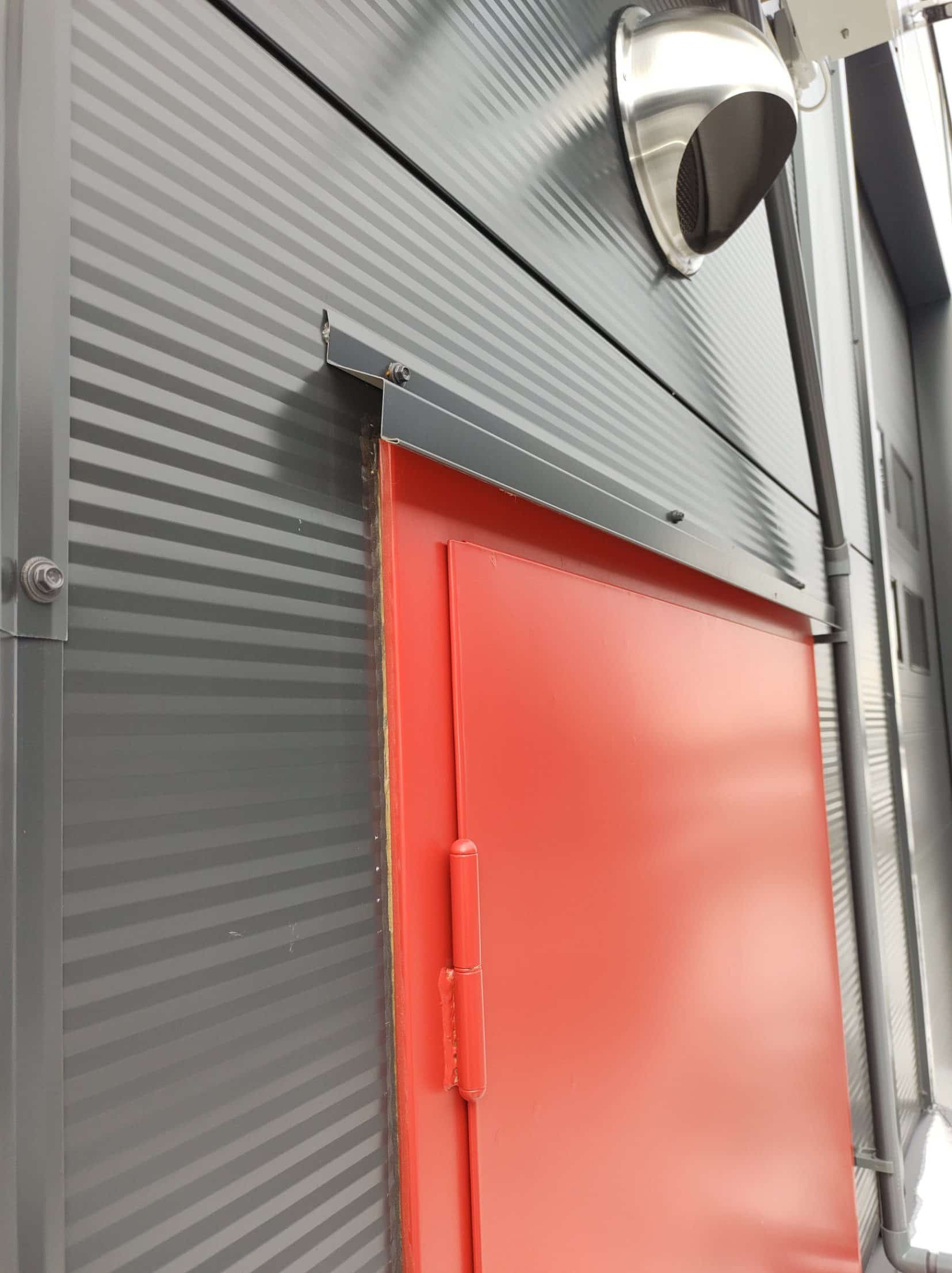 Detail of the metal flashing around a red door in the sandwich panel wall