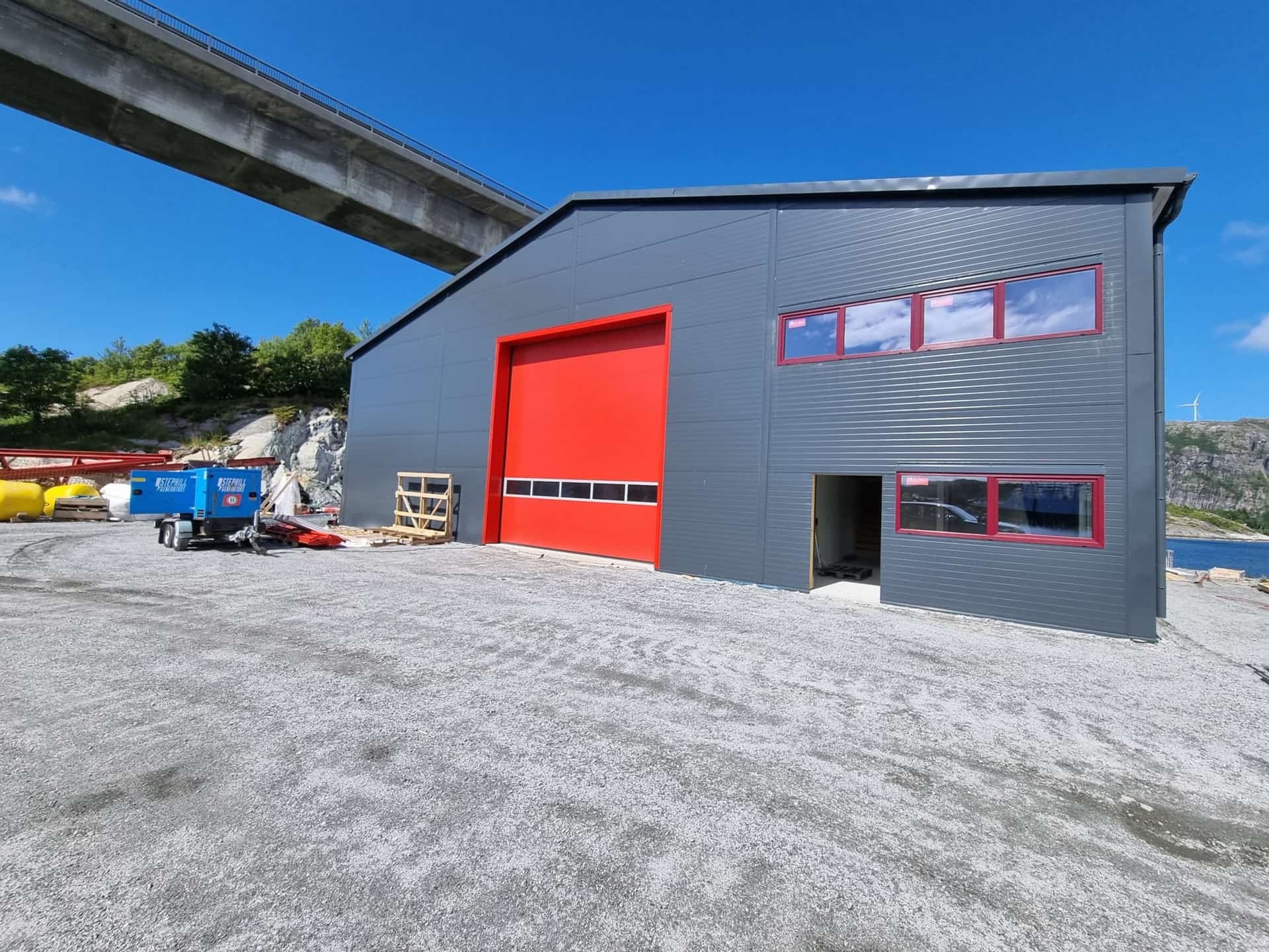 Completed steel building with grey sandwich panel cladding, a red sectional door and windows